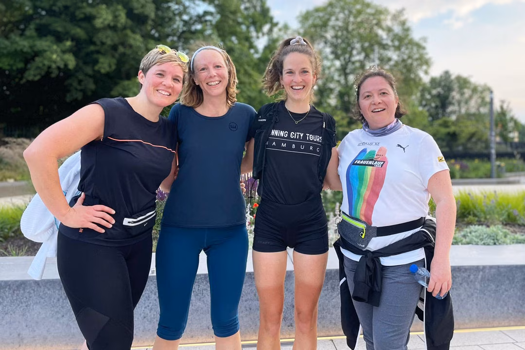 Vier Frauen in Sportkleidung, davon eine Laufführerin von Running City Tours, stehen vor einem Park und lachen.