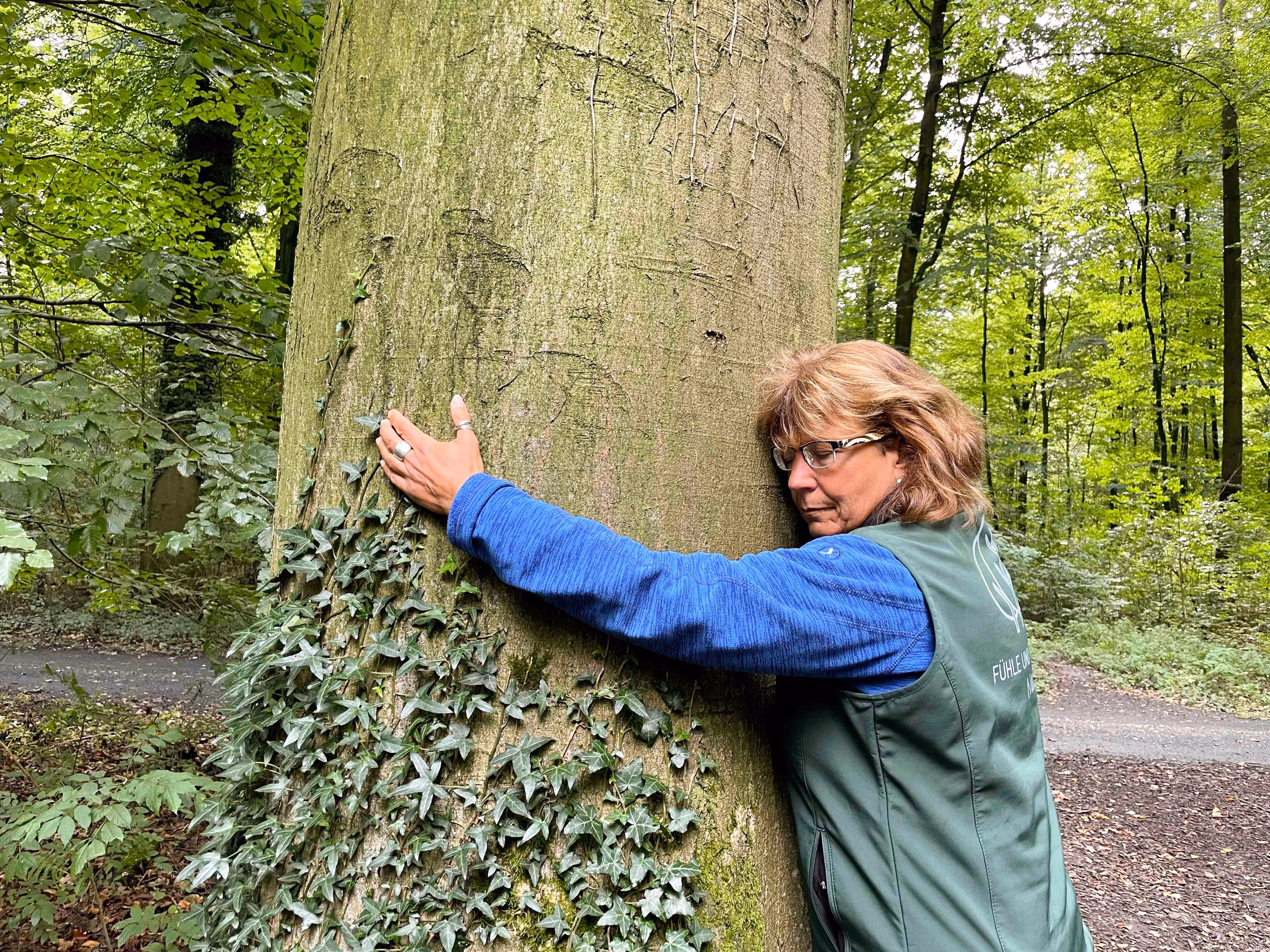 Eine Frau umarmt während eines Waldbaden-Retreats einen Baum