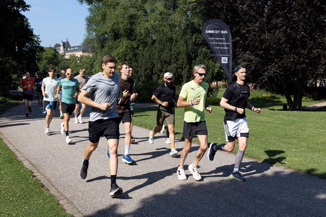Eine Gruppe Menschen joggt durch einen Park, vorne der Guide von Running City Tours mit Banner auf dem Rücken.