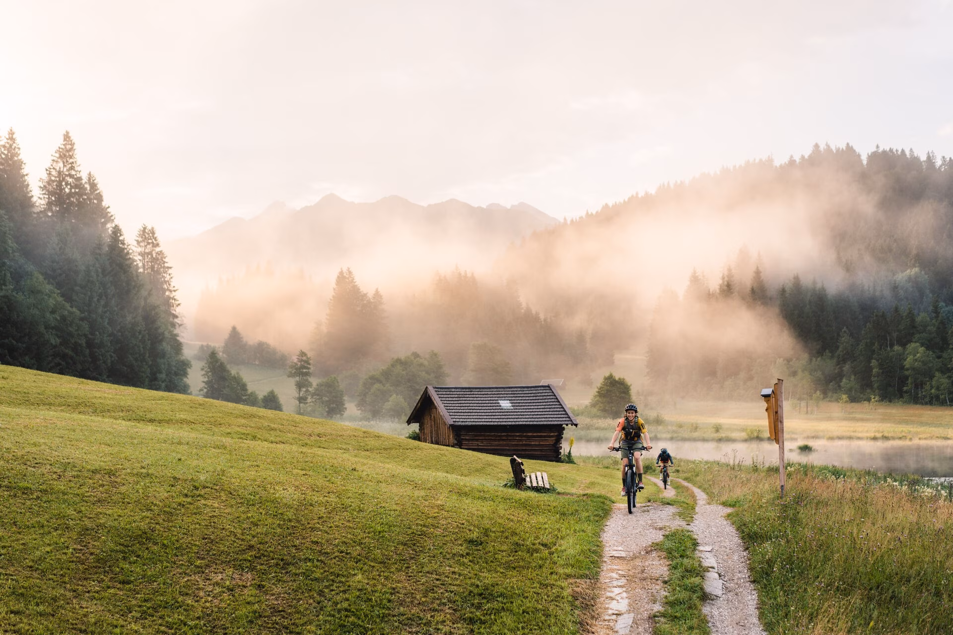 Bayerische Berglandschaft mit Hütte und zwei Radfahrern mit E-Mountainbike