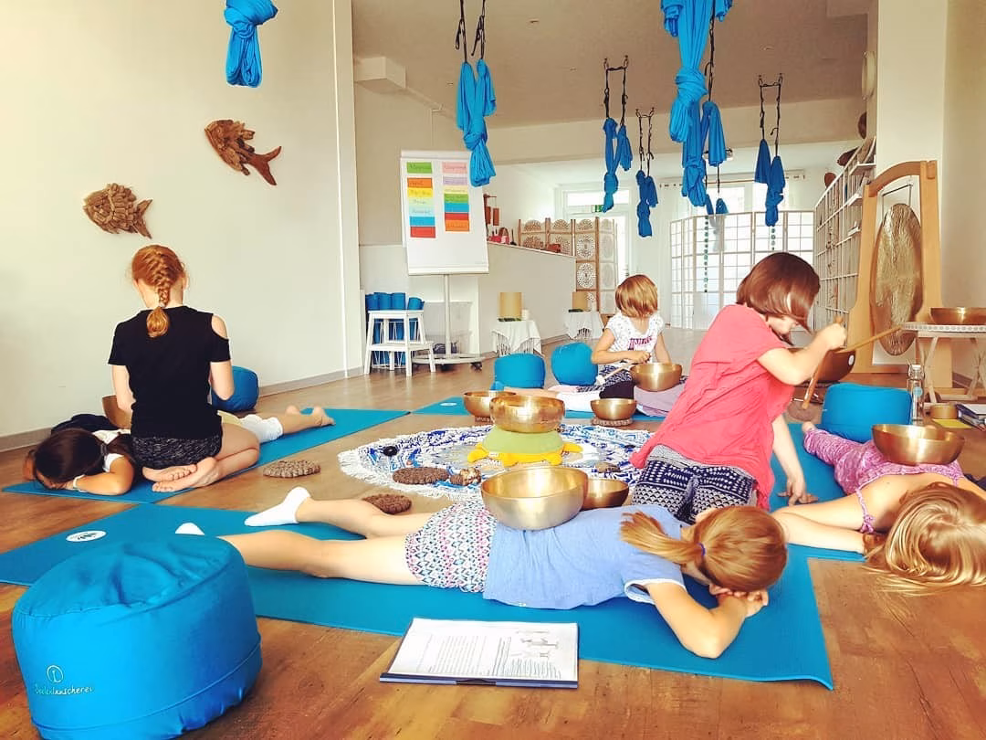 Kinder liegen in einem Raum auf Yoga-Matten und haben Klangschalen auf dem Rücken
