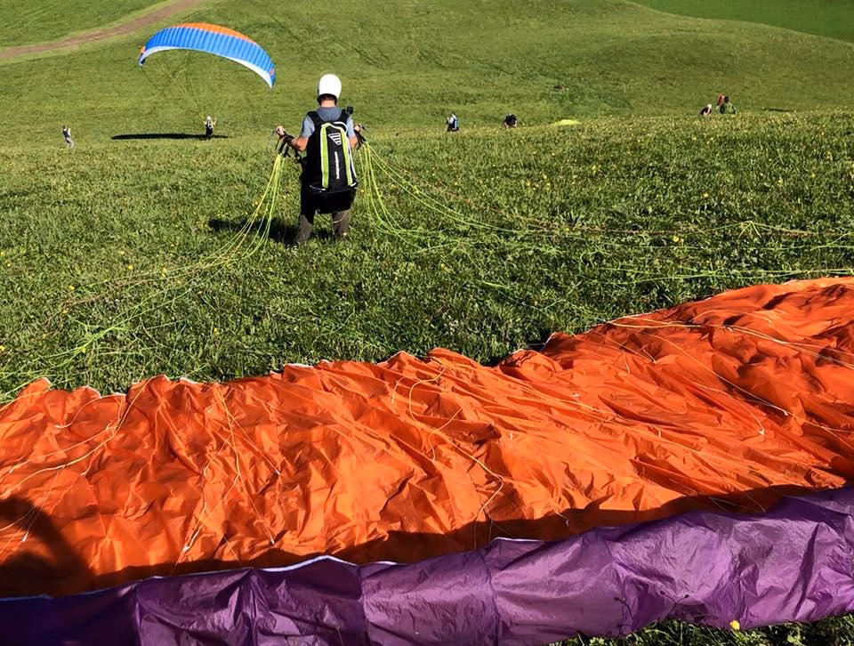 Eine Person an einem Übungshang mit Gleitschirm, der hinter ihr auf dem Boden liegt