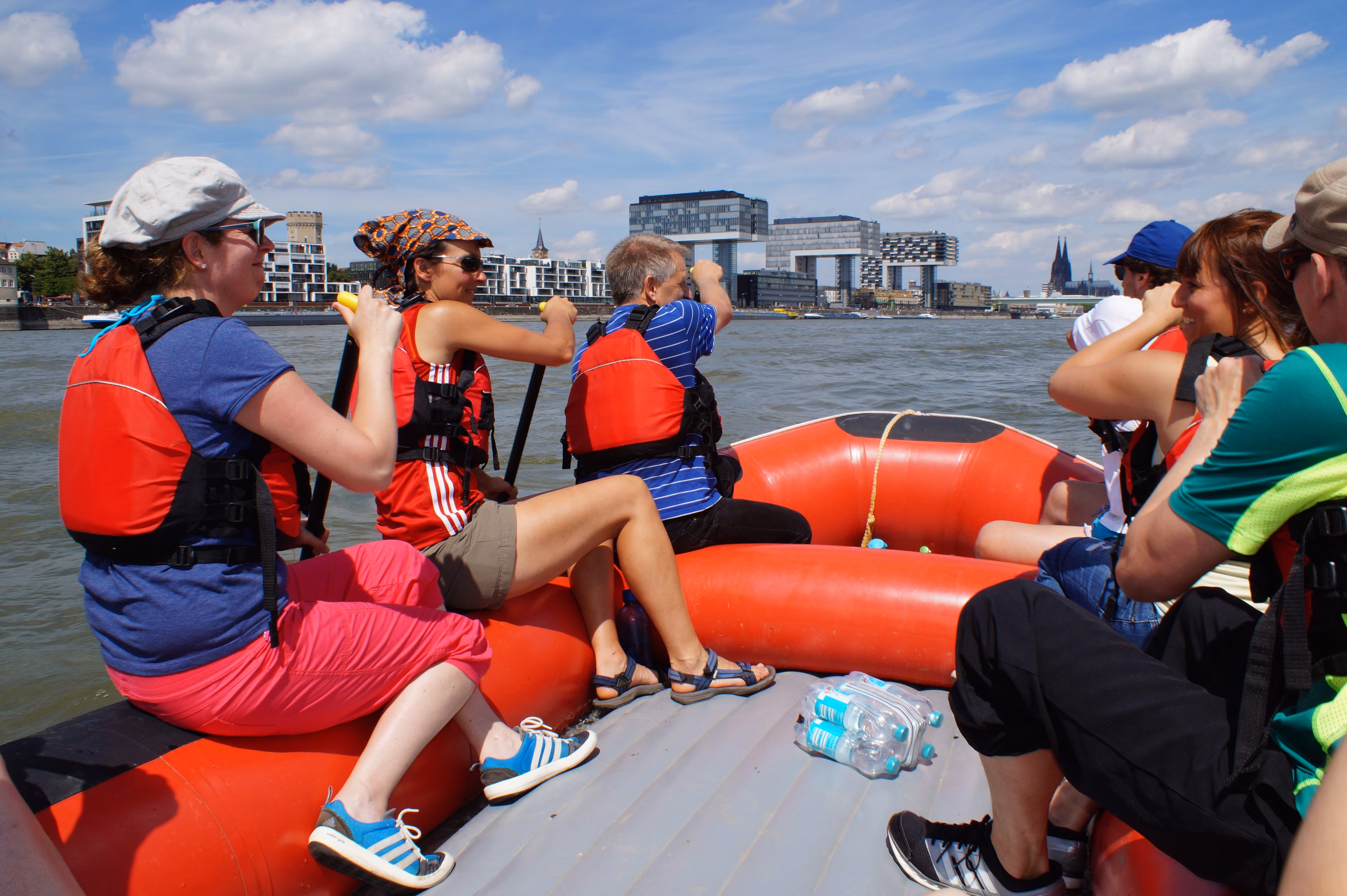 Teilnehmende einer Rafting-Tour in Köln paddeln mit einem Raft auf dem Rhein
