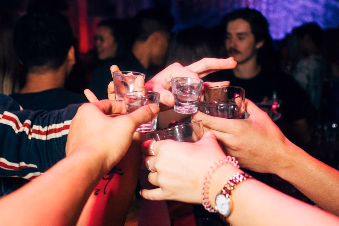 Menschen stoßen mit kleinen Shot-Gläsern auf einer Silvesterparty an.