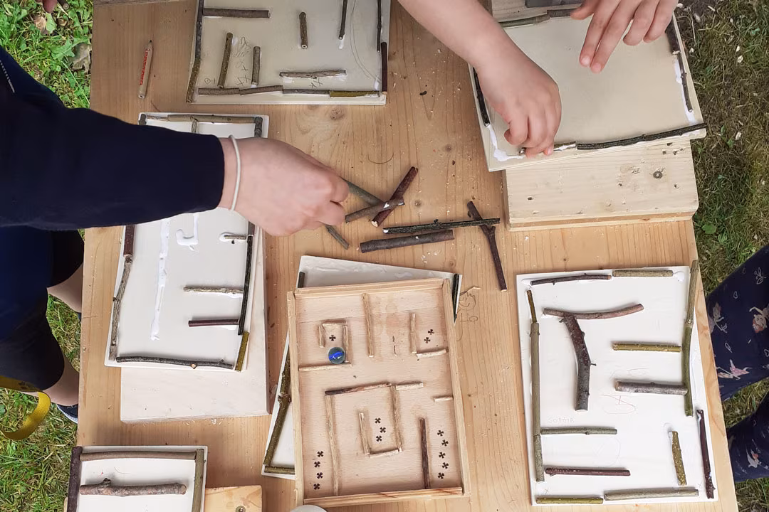 Familien-Holzwerkstatt: Kinder gestalten kreative Holzlabyrinthe mit Zweigen und bauen eigene Spiele in der Werkstatt.