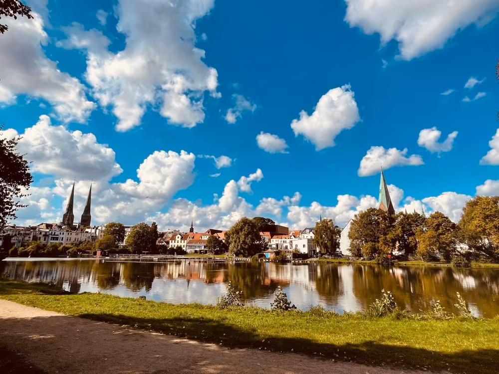 Eine Ansicht der Stadt Lübeck hinter einem von Bäumen umstandenen See