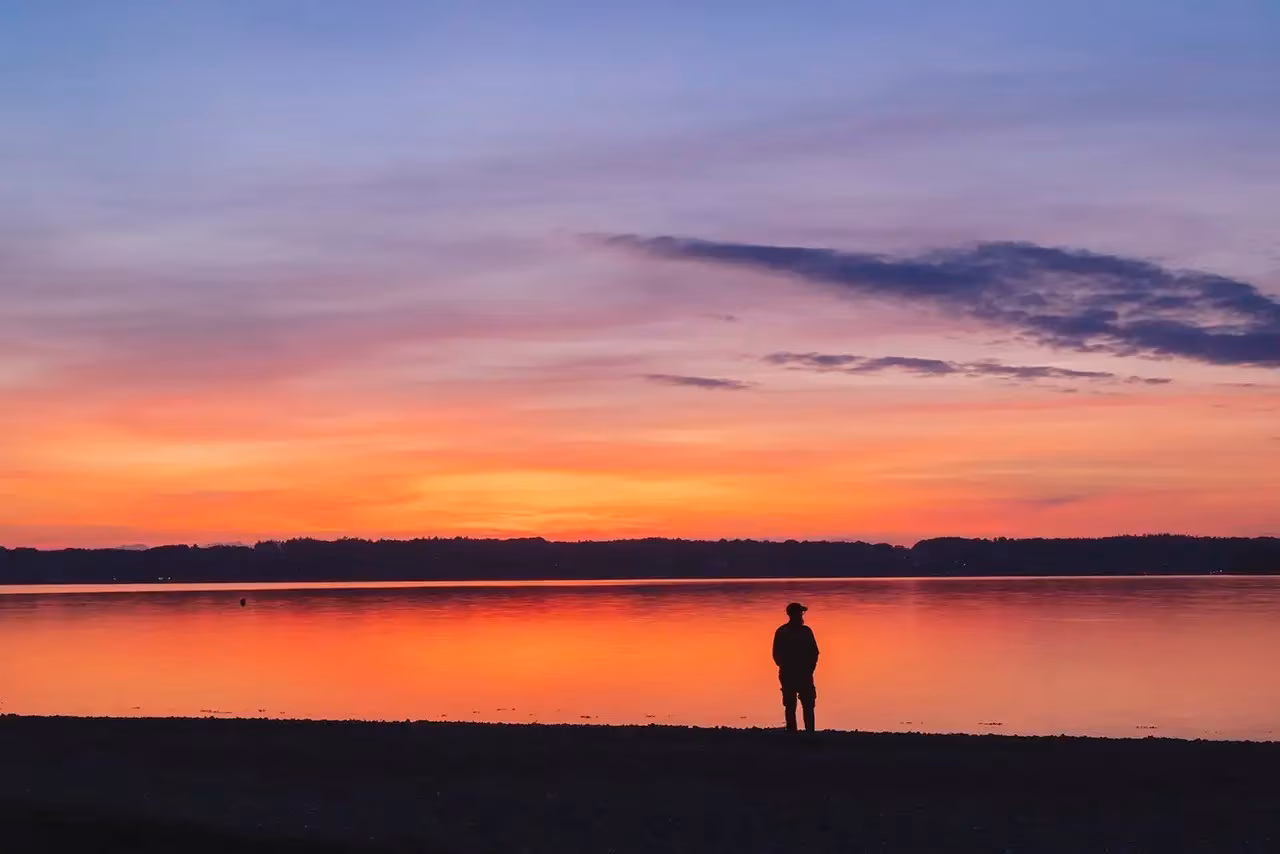 Eine Person steht bei Sonnenuntergang an einem See