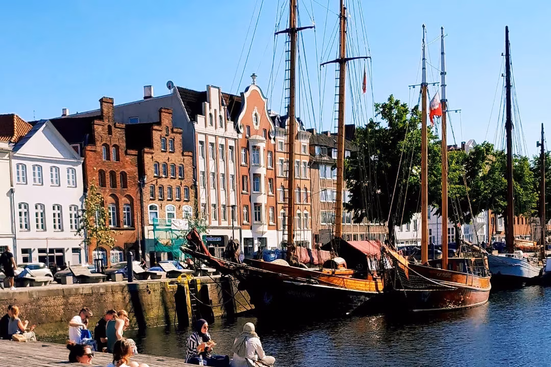 Möglicher Stopp der Radtour: Historische Lübecker Häuser am Hafen mit segelnden Traditionsschiffen und Menschen am Ufer.