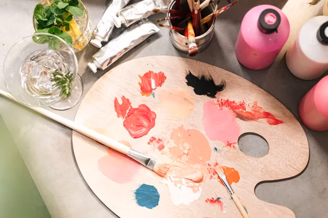 Pinsel, Farben und eine Mischschale aus Holz auf einem Tisch bei der ArtNight.
