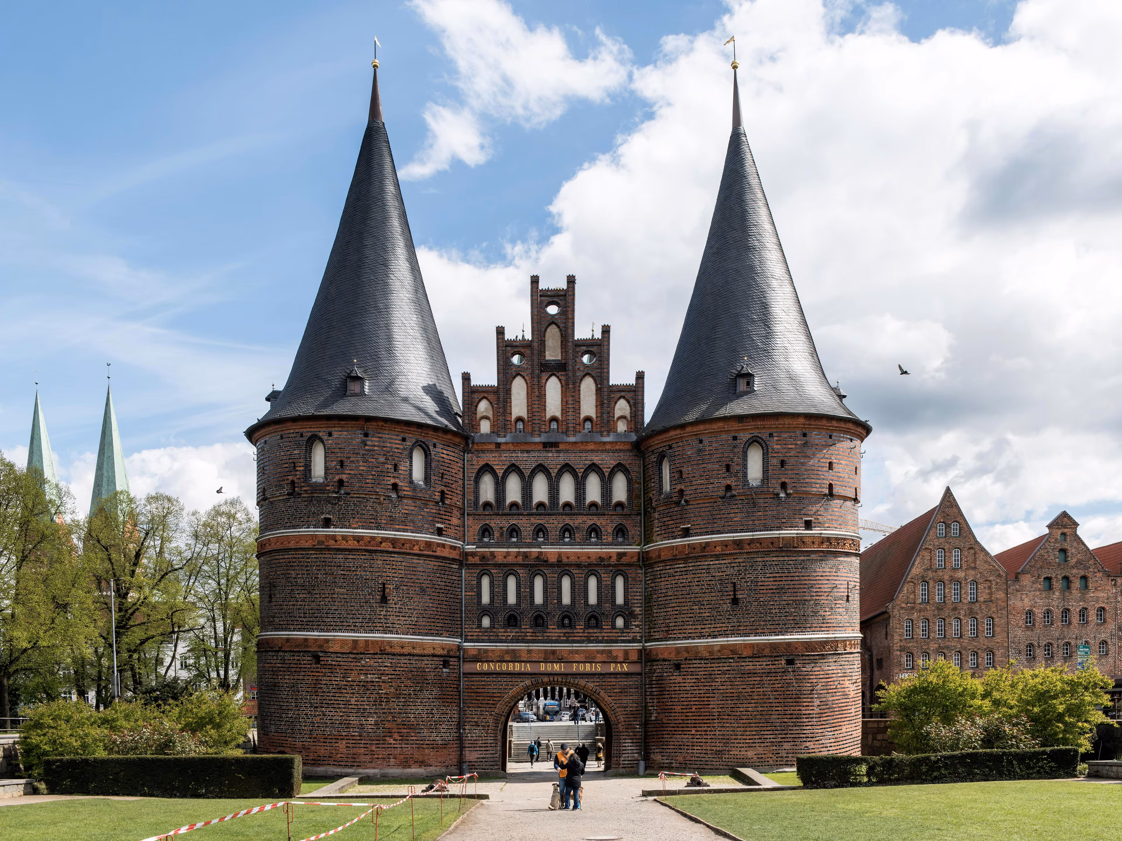 Das Holstentor in Lübeck mit zwei Türmen vor blauem Himmel, davor eine grüne Wiese.