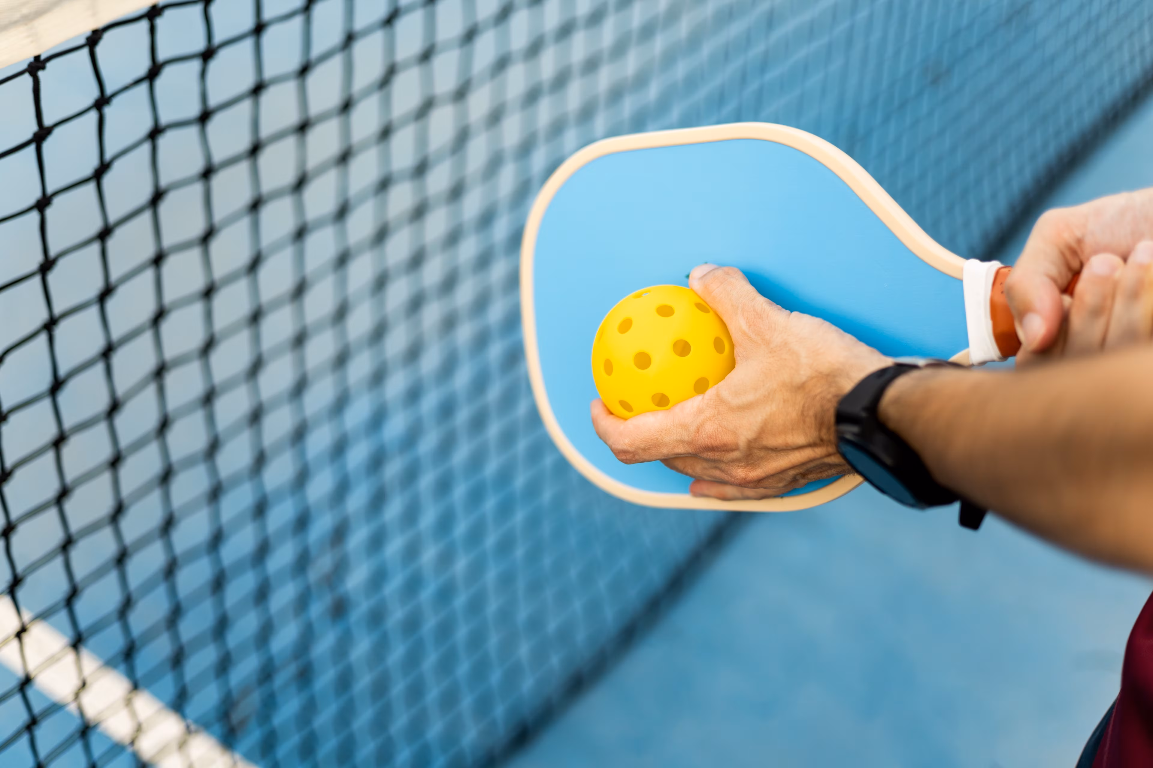 Schläger und Hand, die einen Pickleball hält