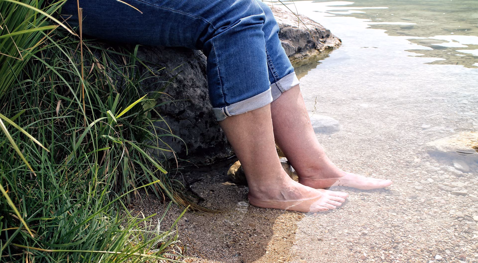 Eine Person sitzt auf einem Felsen am Fluss und hält die nackten Füße ins Wasser