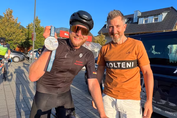 Ein Mann in Rennradkleidung auf seinem Rennrad hält seine Medaille beim Belchen Hoch 3 in die Kamera. Daneben ein Freund.