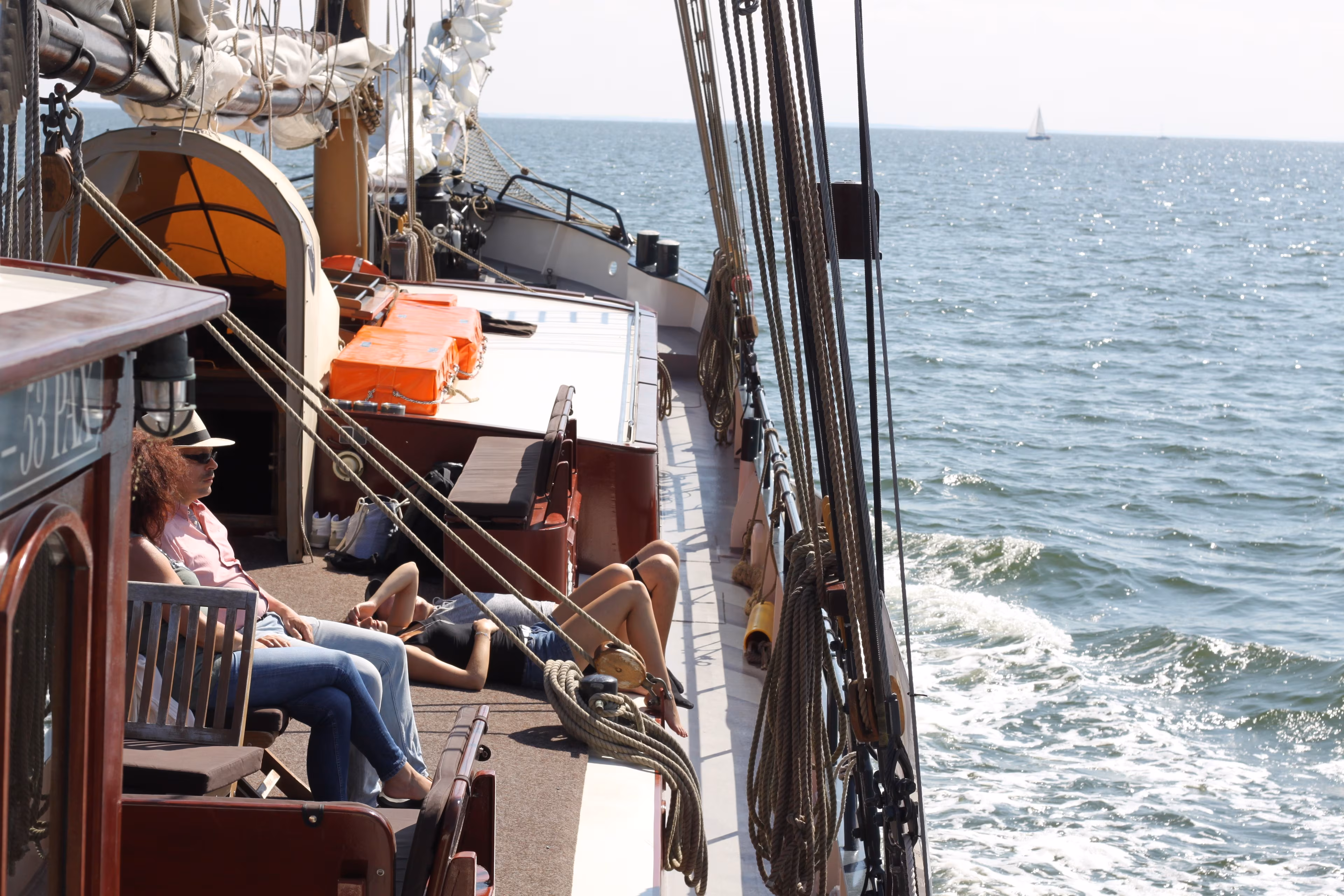 Personen sitzen bei einem Segeltörn entspannt an Deck der „Weissen Düne“ auf der Ostsee