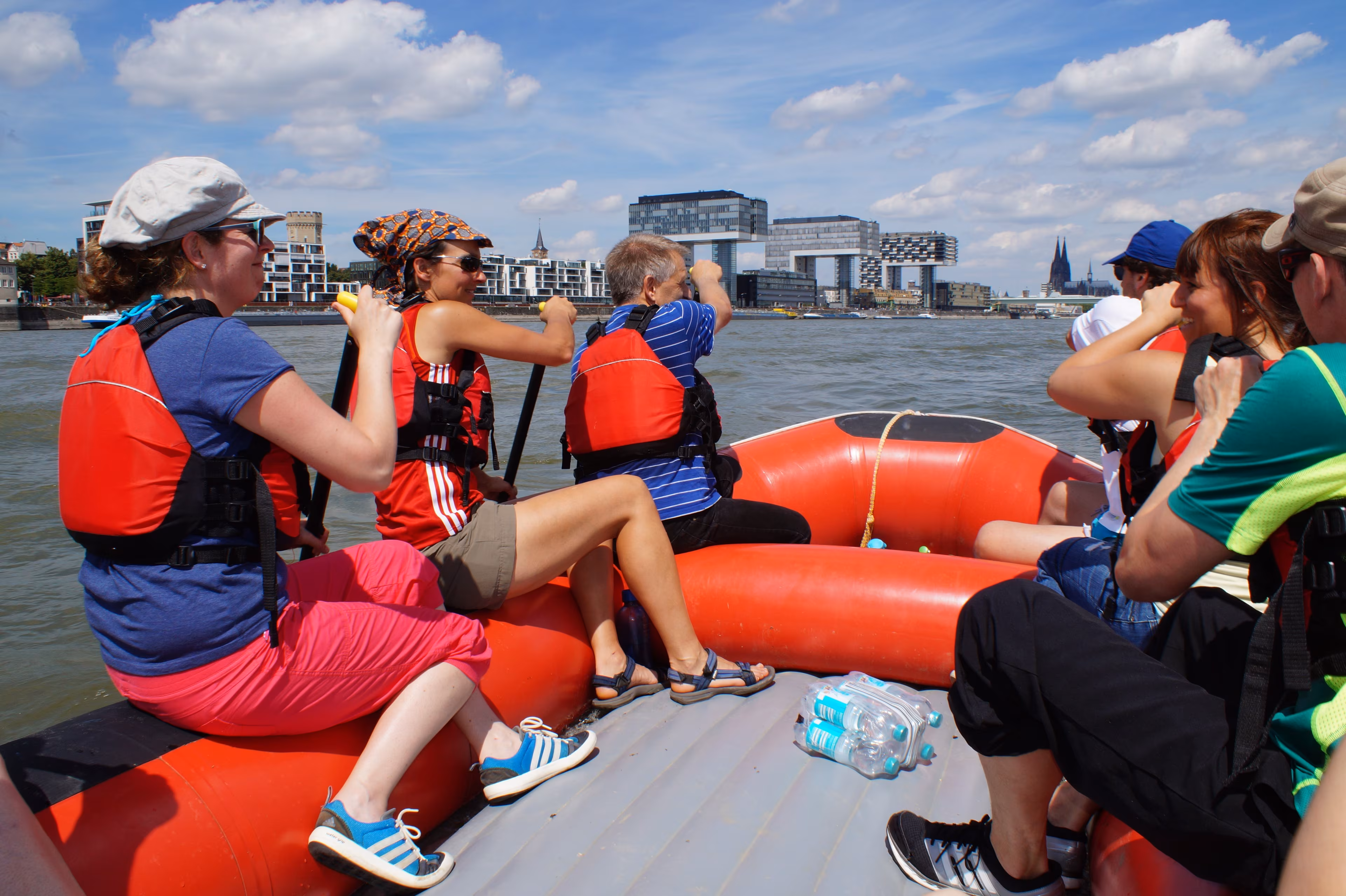 Teilnehmende einer Rafting-Tour in Köln paddeln mit einem Raft auf dem Rhein