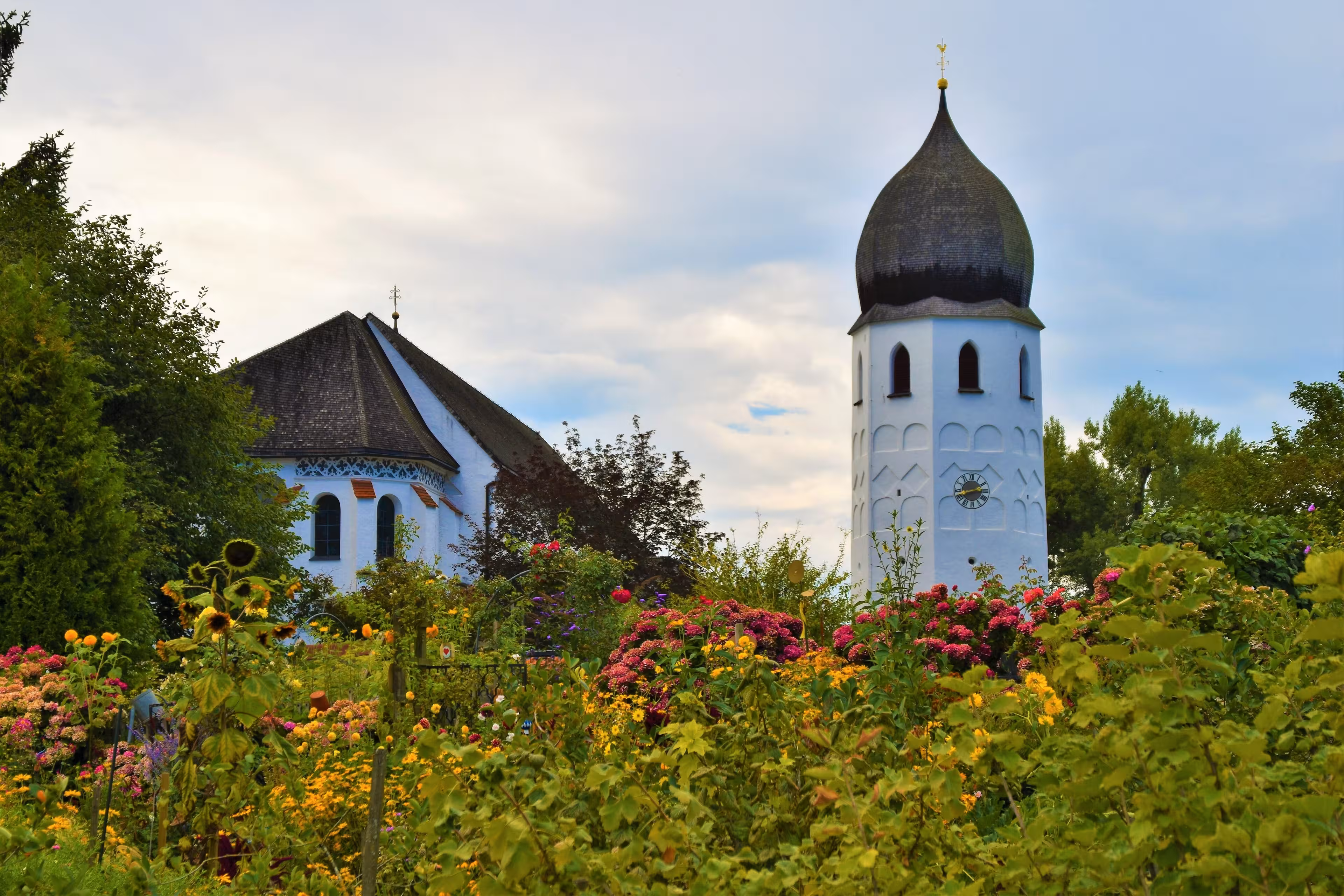 Bunte Blumen in einem Garten auf der Fraueninsel mit dem Kloster Frauenchiemsee im Hintergrund