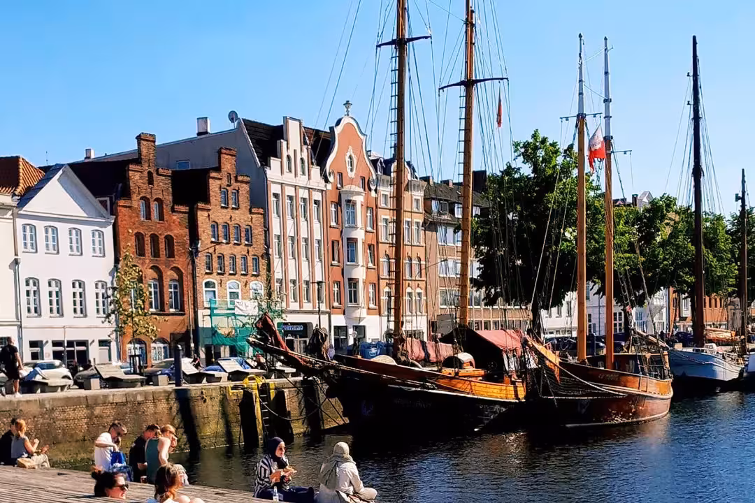 Möglicher Stopp der Radtour: Historische Lübecker Häuser am Hafen mit segelnden Traditionsschiffen und Menschen am Ufer.