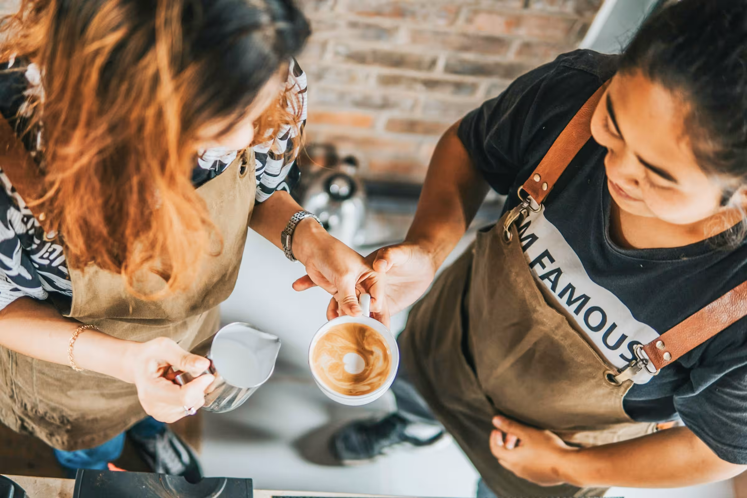 Zwei Personen gießen geschäumte Milch bei einem Barista-Workshop
