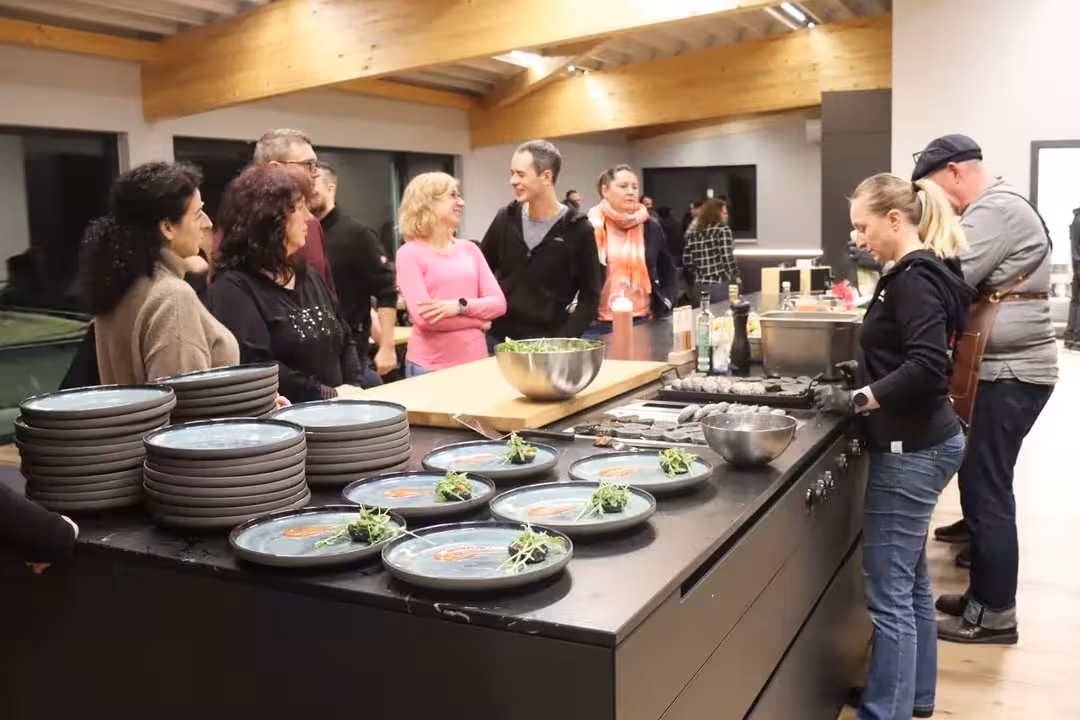 Mehrere Menschen stehen in der Eventküche beim Afterwork Burger-Grillkurs und schauen dem Profikoch zu.