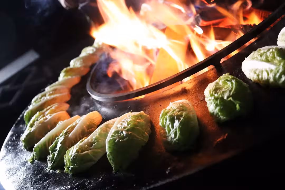 Mehrere Kohlköpfe auf gusseisernem Feuerring beim Afterwork Burger-Grillkurs. Im Hintergrund lodert das Feuer.
