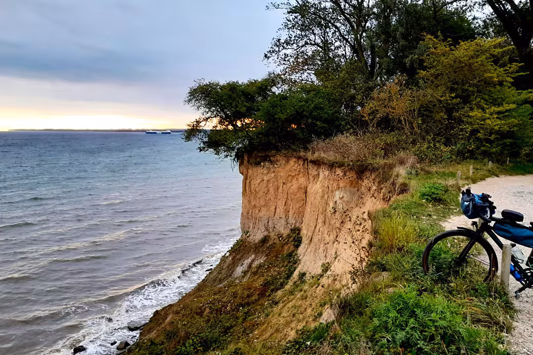 Steilküste an der Ostsee bei ruhiger Brandung, ein Fahrrad steht am Rand des Küstenwegs.