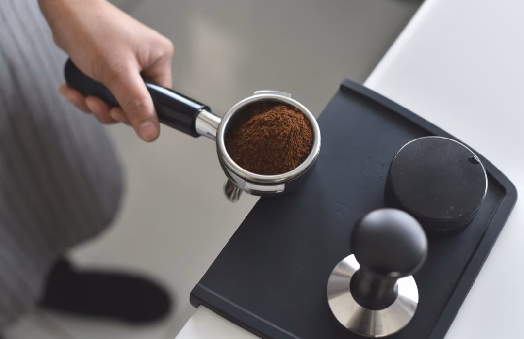 Frau mit Kaffeekolben, darin frisch gemahlener Kaffee. Davor ein Tamper.