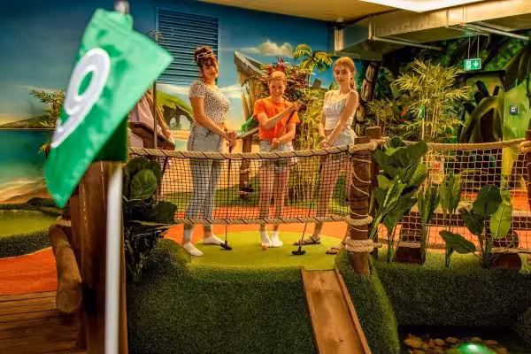 minigolf-fahne-im-vodergrund-drei-fraue-mit-minigolfschlägern