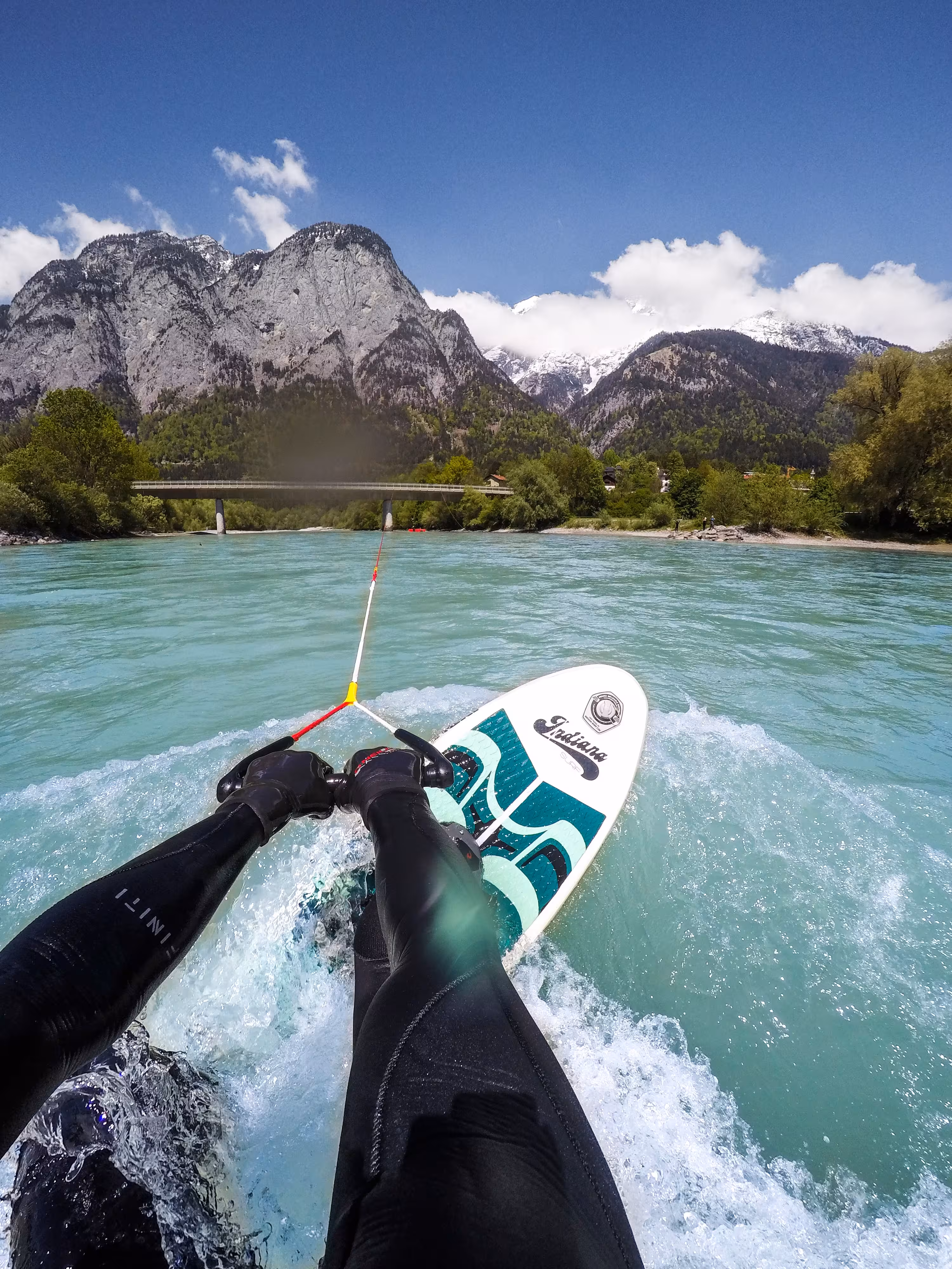 Blickwinkel einer Person beim Upstream-Surfing, die ein Seil in den Händen hält, das an einer Brücke befestigt ist