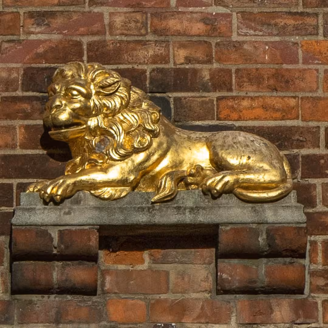 Goldene Löwenfigur auf einer Backsteinwand in Lübeck – eines der versteckten Details der St.-Marien-Tour.