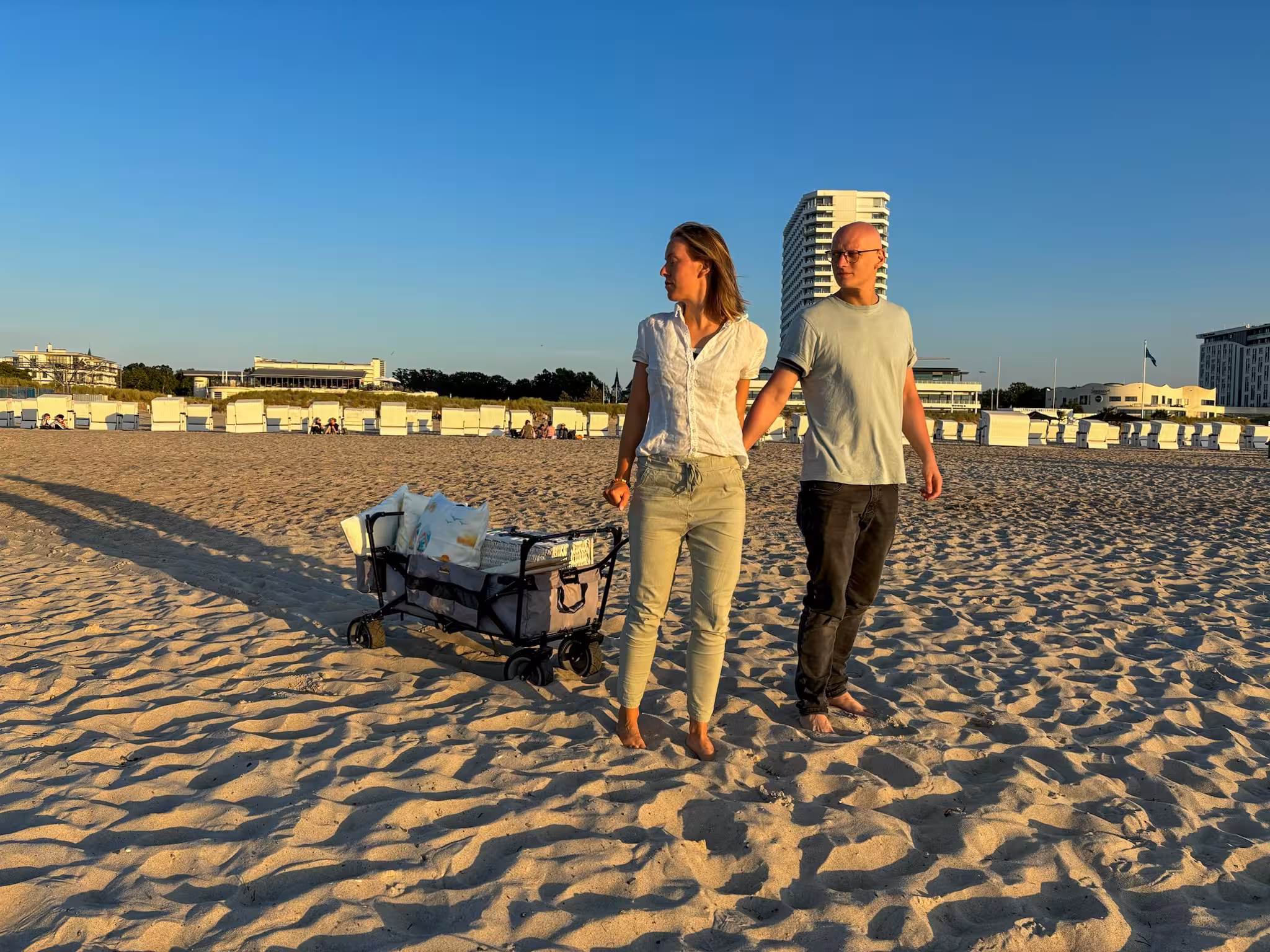 Zwei Personen ziehen einen Bollerwagen mit Picknick-Utensilien am Strand von Warnemünde