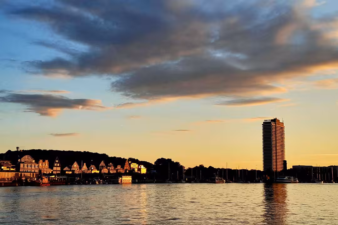 Blick vom Küsten-Fahrradweg au die Skyline von Travemünde mit Promenade im warmen Licht des Sonnenuntergangs.