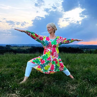 Simone Schmid auf einer Wiese bei Abendstimmung, in der Position des Krieger II.